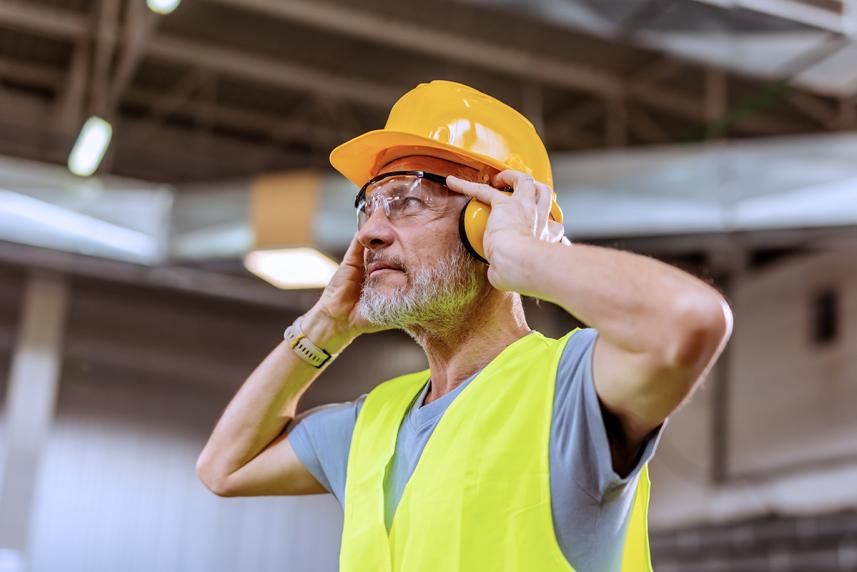 A man with construction gear on, holding headphones over his ears