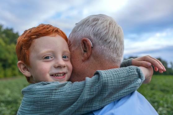 Kid hugging grandpa with hearing aid